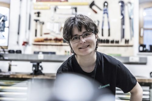 Eine lächelnde Person steht in einer Werkstatt voller Werkzeuge, spezialisiert auf Heiztechnik.