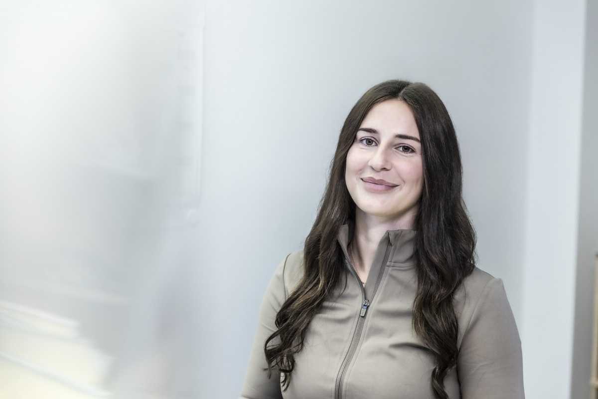 Eine lächelnde Frau steht vor einem hellen Hintergrund und vermittelt Vertrauen in den Bereichen Klimatechnik und Heiztechnik.