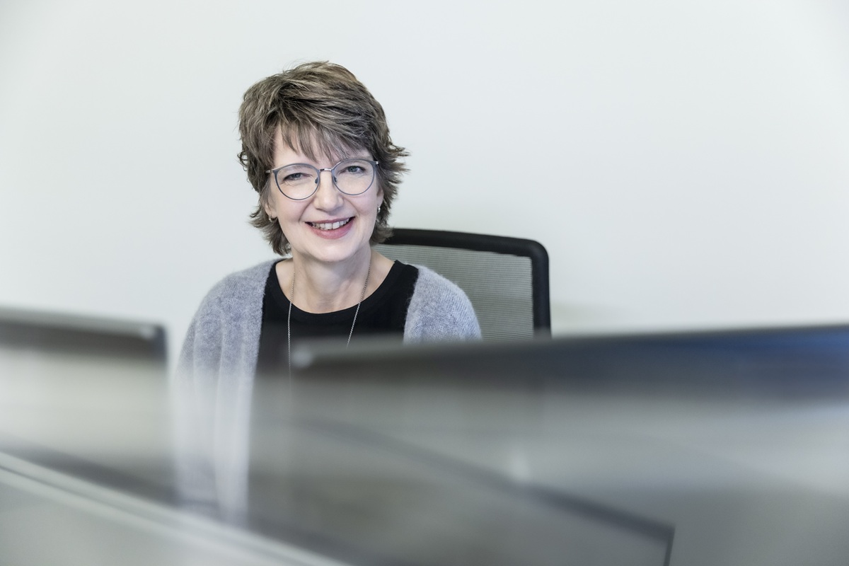 Eine lächelnde Frau sitzt am Schreibtisch und arbeitet an einem Computer, um Projekte in der Sanitär- und Klimatechnik zu planen.