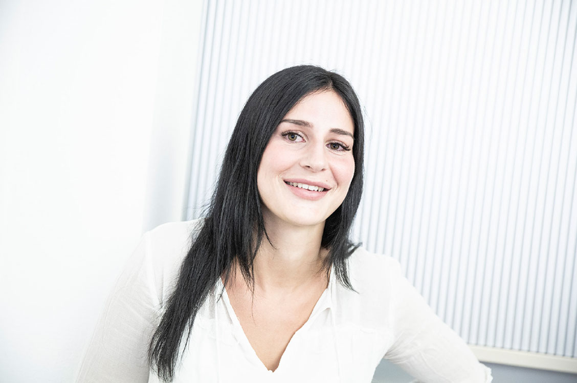 Eine lächelnde Frau in weißer Bluse repräsentiert professionell den Bereich der Klimatechnik mit Freundlichkeit.